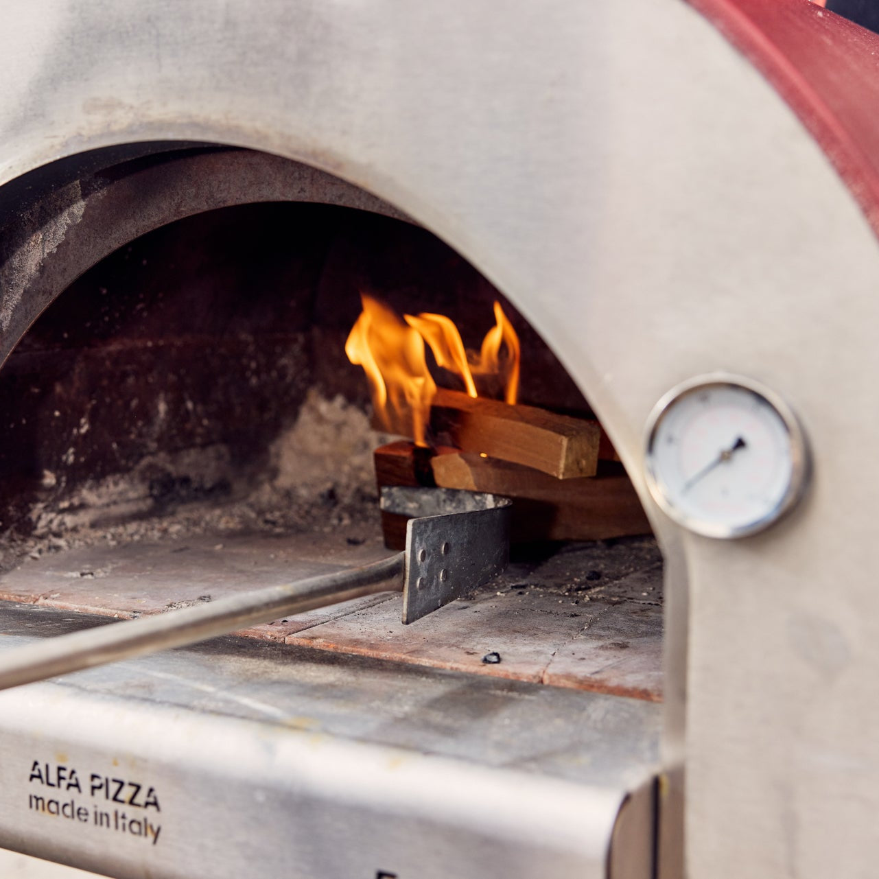 Outdoor pizza oven with flames inside, showing the brand 'Alfa Pizza'.