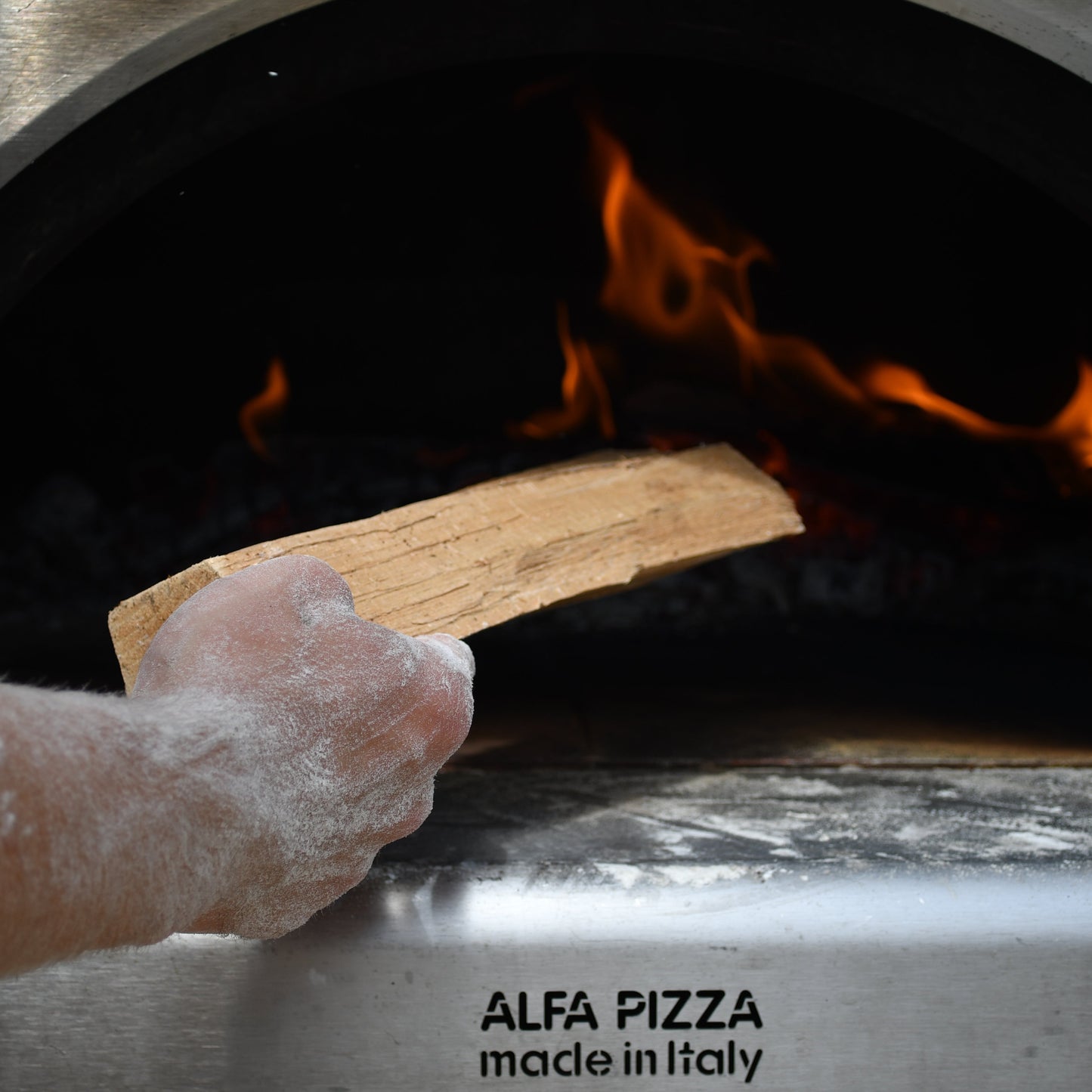 Person using a wooden peel to place pizza into an Alfa Pizza oven.